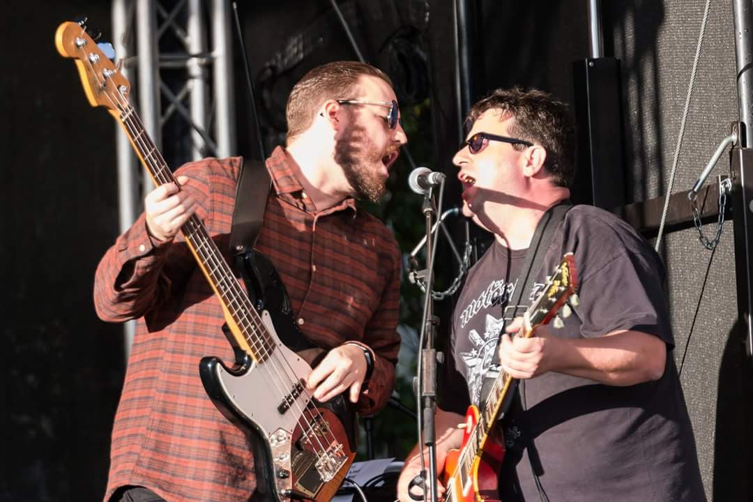 Guido Leidheuser playing guitar and sharing a microphone with a bass player